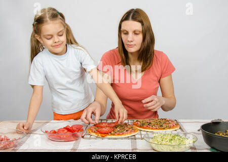 Sechsjährigen Mädchen hilft Mutter verteilt auf Tomaten pizza Stockfoto