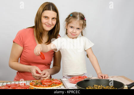 Fünfjähriges Mädchen hilft Mutter auf den Pizzazutaten zu verbreiten Stockfoto