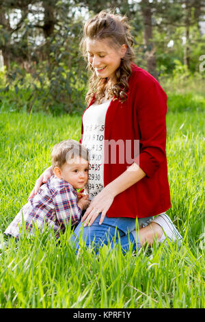 Schöne schwangere Frau mit ihren kleinen Jungen im Freien Stockfoto