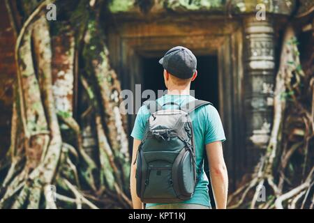 Junger Mann mit Rucksack zu antiken Monumente, die unter den riesigen Wurzeln des Baums in der Nähe von Siem Reap (Angkor Wat) in Kambodscha Stockfoto