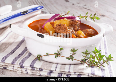 Leckere Gulaschsuppe im weißen Topf auf weißem Hintergrund aus Holz. Kulinarischen traditionelle Gulasch essen. Stockfoto