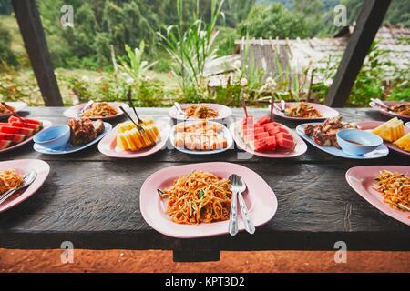 Mittagessen in der Mitte des Dschungels. Der Tisch voller Lebensmittel und Früchte. Traditioal Pad Thai, Frühlingsrollen, Melone und Ananas. Provinz Chiang Mai, Th Stockfoto