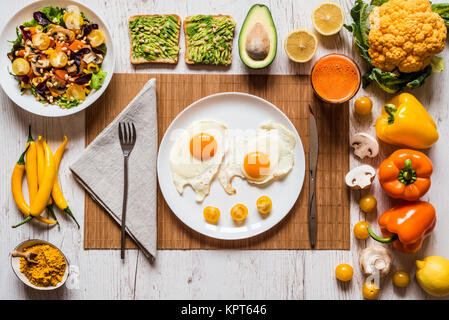 Gesunde Lebensmittel für Frühstück. Spiegeleier, vegan avocado Sandwiches, Gemüse, Salat, Karotten frische Säfte und verschiedene bunte Gemüse auf dem weißen Holz- Hintergrund. Stockfoto