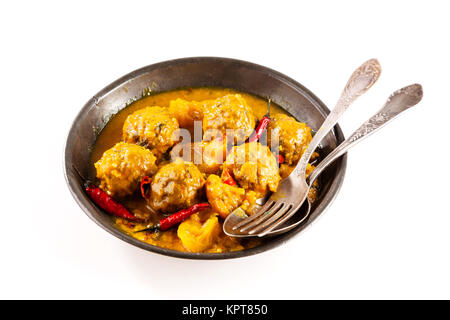 Hohe Betrachtungswinkel der traditionellen Tajine Berber Schüssel Fleischbällchen erstickt in der würzigen Gelben Curry Sauce mit heissen roten Paprika und serviert im flachen Schüssel mit Besteck auf weißem Hintergrund Stockfoto