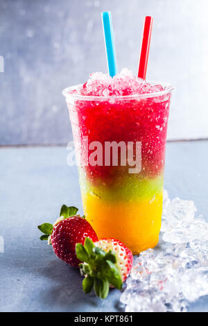 In der Nähe der bunten Regenbogen Layered gefrorenes Obst Slush Granita Drink auf Metall Zähler in Kunststoff entfernt Schale nehmen mit Trinkhalm und durch frische Erdbeeren und Eis umgeben Stockfoto