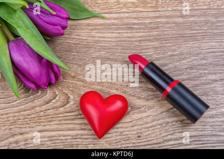 Lippenstift, rote Herzen und lila Tulpen auf einem hölzernen Hintergrund Stockfoto