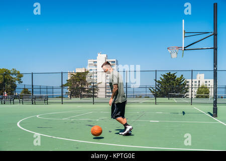 Junger Mann spielt Basketball an der öffentlichen Alice Marmor Tennisplätze in San Francisco, Kalifornien. Stockfoto