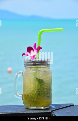 Große Gläser Becher Stil vollen Glas frisch gefrorenen Mojito mit Metallkappe Deckel, Stroh und lila Orchidee Blume im Café am Strand Stockfoto