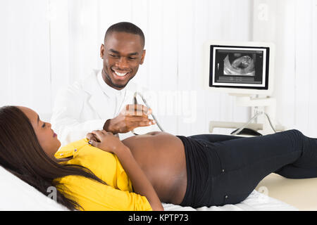 Happy African American Frauenarzt bewegte Ultraschallaufnehmer auf schwangeren Bauch der Frau Stockfoto