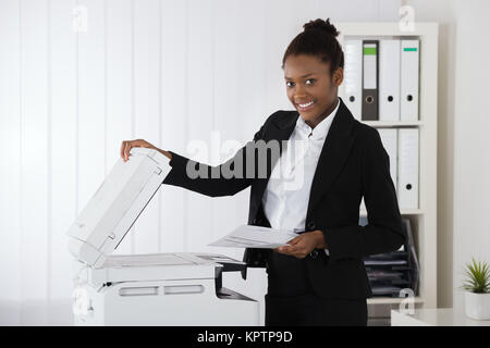 Lächelnden jungen afrikanischen Geschäftsfrau Einlegen von Papier für Kopierer im Büro Stockfoto