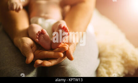 Mutter des neugeborenen Babys Füße. Kleine Füße in der Hand der Frau. Stockfoto