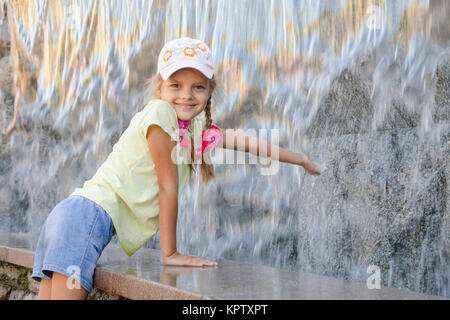 Mädchen im Sommer-Kleider mit einem Lächeln erstreckt sich seine Hand auf den künstlichen Wasserfall Wasser Stockfoto