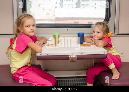 Zwei kleine Mädchen im Zug sitzen am Tisch in der Außenborder zweiter Klasse Wagen in der gleichen Kleidung Stockfoto