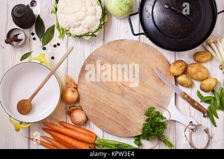 Hohen Winkel noch Leben Blick auf ein Schneidbrett, Messer und Wok Pfanne durch frisches rohes Gemüse auf lackierten Holz Tisch umgeben - Vorbereitung einer Mahlzeit mit rohen Zutaten Stockfoto