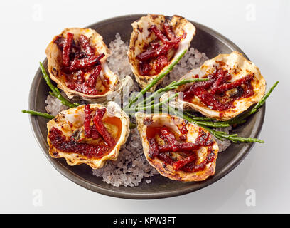 Nahaufnahme noch Leben auf der Platte der Austern Kilpatrick vorbereitet mit Speck und Käse serviert mit Salz Garnitur auf weißem Hintergrund Stockfoto
