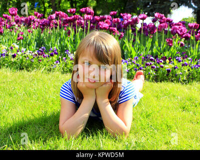 Schule Mädchen legt auf das Gras und neben Tulpen Stockfoto