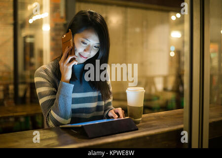 Frau sprechen sie mit Handy und Verwendung der Tablet bei Kaffee Tasse Stockfoto