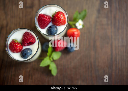 Natürliche Joghurtgläser mit frischen Beeren auf rustikalem Holz Stockfoto