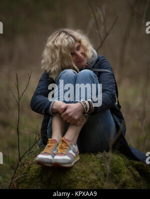 Blonde Mädchen sitzt auf dem Baumstumpf im Wald das Gleiche wie Bild Alyonushka von Vasnetsov Stockfoto