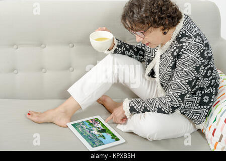 Schöne, reife Frau mit einem Tablett auf der Couch Stockfoto