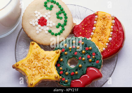 Drei Weihnachten schneiden Sie Cookies auf einer Glasplatte mit einem Glas Milch Stockfoto