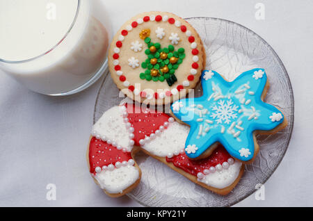 Drei Weihnachten schneiden Sie Cookies auf einer Glasplatte mit einem Glas Milch Stockfoto