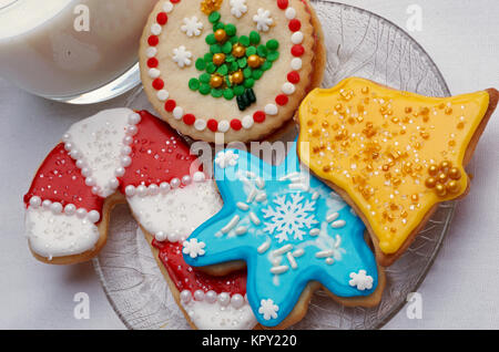 Drei Weihnachten schneiden Sie Cookies auf einer Glasplatte mit einem Glas Milch Stockfoto