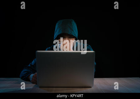 Hacker in einem dunklen Pulli Vor dem Notebook sitzen. Computer Datenschutz Angriff Stockfoto