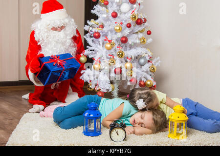 Santa Claus in New Years Eve Geschenke legt und schaute auf die gefallenen schlafend vor Weihnachtsbaum zwei Kindern Stockfoto