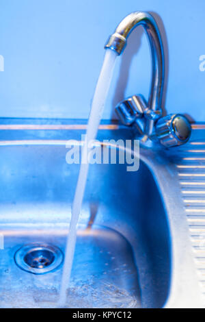 Ein sauberes, transparentes frisches Wasser fließt aus dem Stahl glänzend in ein Waschbecken aus Edelstahl in blau Tönen tippen. Wasser fließt in die Öffnung für Th Stockfoto