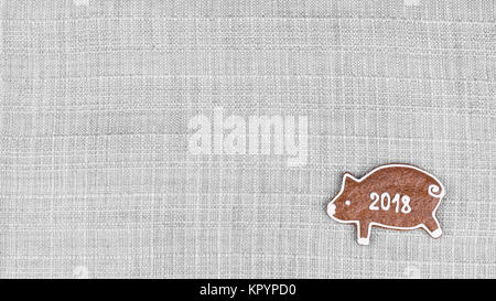 Piggy aus dem Weihnachten Lebkuchen bringt ein frohes neues Jahr. Hintergrund mit Stoff Textur und niedlichen kleinen Schweinchen mit dem 2018 schreiben. Stockfoto