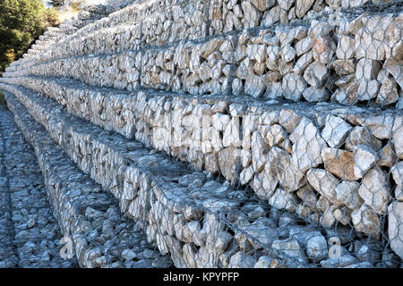 Eine Reihe von trat zurück Gabionen, Stein gefüllt Käfige, Linie a Mountain Road Schutz der Damm von Erosion und zum Schutz der Straße. Stockfoto