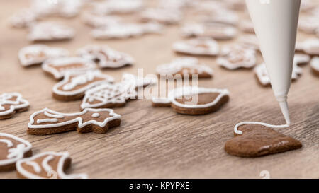 Nahaufnahme der Dekoration Weihnachten Lebkuchen in Herzform. Malerei von Gebäck mit Zuckerglasur Tasche mit Zucker Zuckerguß auf Holz. Kleine Tiefe der Schärfe. Stockfoto