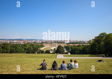 Gruppe von Menschen, die auf Gras mit Blick auf das Schloss Schönbrunn und der Stadt Wien von Schönbrunn Park Hill in Wien, Österreich, Europa sitzen Stockfoto