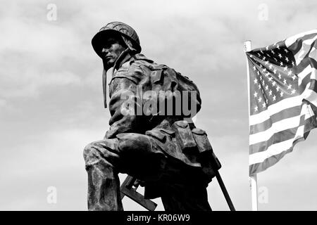 Bronze Statue eines Iron Mike, ein Soldat der amerikanischen Armee Besitz einer Waffe mit der Flagge der Vereinigten Staaten von Amerika. La Fiere Brücke, Sainte-Mere- Stockfoto