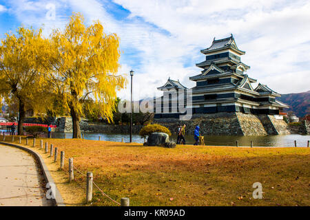Der Bergfried Schloß Matsumoto oder Krähe Schloss im Herbst, einem der berühmtesten historischen Schlössern von Japan, mit einem gelben Baum im Vordergrund. Stockfoto