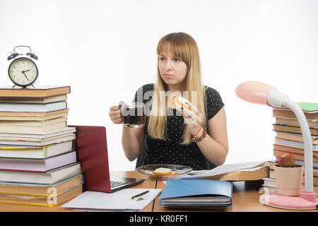 Hungrige junge Lehrer sitzen müde mit Sandwich und Kaffee Stockfoto