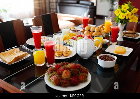 Gesundes Frühstück mit Brot und Wurst auf dunklen Holztisch. Tropische Früchte, frisch gepressten Orangensaft, Toast und Croissants für Familie Frühstück o Stockfoto