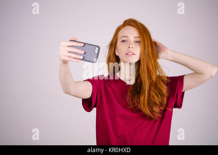Rothaarige Mädchen nimmt einen selfie. Sie hat lange rote Haare. trägt Marsala t-shirt Stockfoto