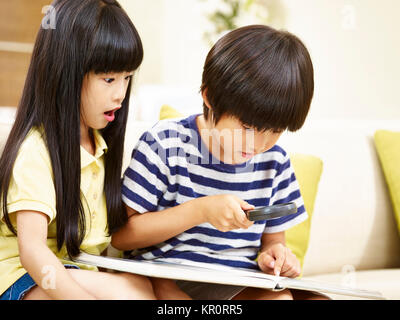 Zwei asiatische Kinder Jungen und Mädchen sitzen auf der Couch spielen mit einer Lupe. Stockfoto