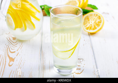 Ein Becherglas und einen Krug kalten Limonade auf einem weißen Hintergrund Holz umgeben von Zitronen Stockfoto