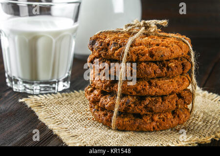 Hausgemachte oatmeal Cookies. Ein Stapel von Cookies mit String einen Sack auf braunem Holz- Tabelle gebunden. Milch im Hintergrund Stockfoto