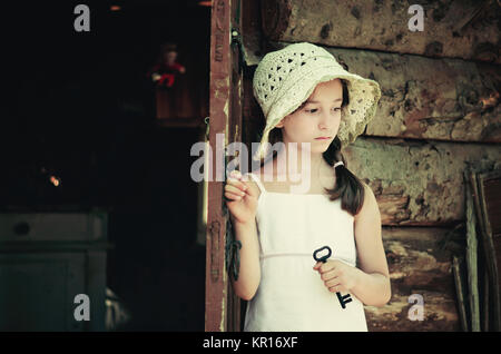 Hübsche junge Mädchen, der an der Tür außerhalb einer alten Holzhütte und halten Sie eine Taste. Retro und Vintage Look, nostalgische Stimmung. Stockfoto