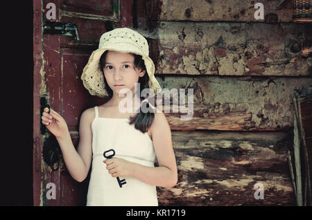 Hübsche junge Mädchen, der an der Tür außerhalb einer alten Holzhütte und halten Sie eine Taste. Retro und Vintage Look, nostalgische Stimmung. Stockfoto