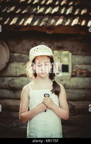 Hübsche junge Mädchen stehend außerhalb einer alten Holzhütte und halten Sie eine Taste. Retro und Vintage Look, nostalgische Stimmung. Stockfoto