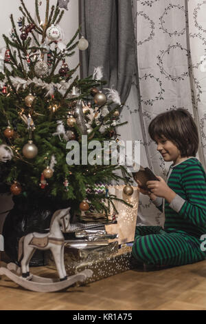 Junge im Schlafanzug auf Geschenke unter dem Weihnachtsbaum Stockfoto