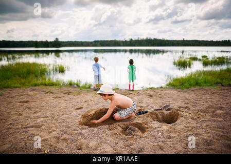 Junge spielt in den Sand und zwei Kinder an einem See Stockfoto