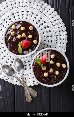 Süße Schokolade Pudding mit Haselnüssen, Minze und Himbeeren in der Nähe eingerichtet - auf den Tisch. Vertikal oben Ansicht von oben Stockfoto