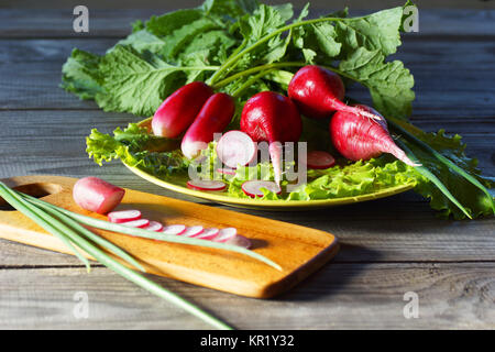 Stillleben mit Feder Gemüse - Radieschen, Salat und grüne Zwiebeln. Radieschen und Kopfsalat Blätter liegen auf einer Platte. Sauber Radieschen für die Verwendung in Lebensmitteln zubereitet. Stockfoto