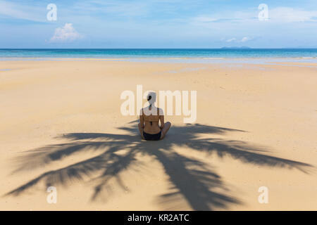 Junge Frau sitzen im Schatten der Palmen am tropischen Strand auf Koh Kood Island, Thailand Stockfoto